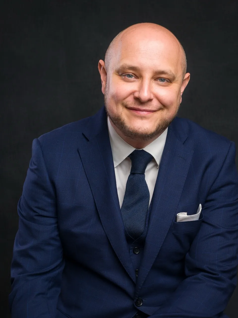 Adam Lord in a navy suit, seated, smiling at the camera
